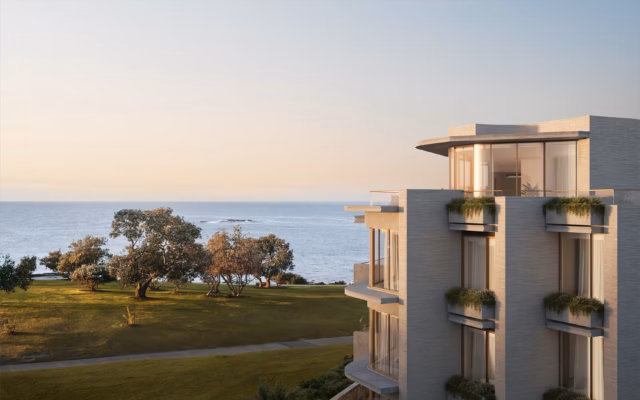 A contemporary low-rise apartment building with balconies and planter boxes, overlooking a grassy coastal area and the ocean at Coogee, New South Wales.